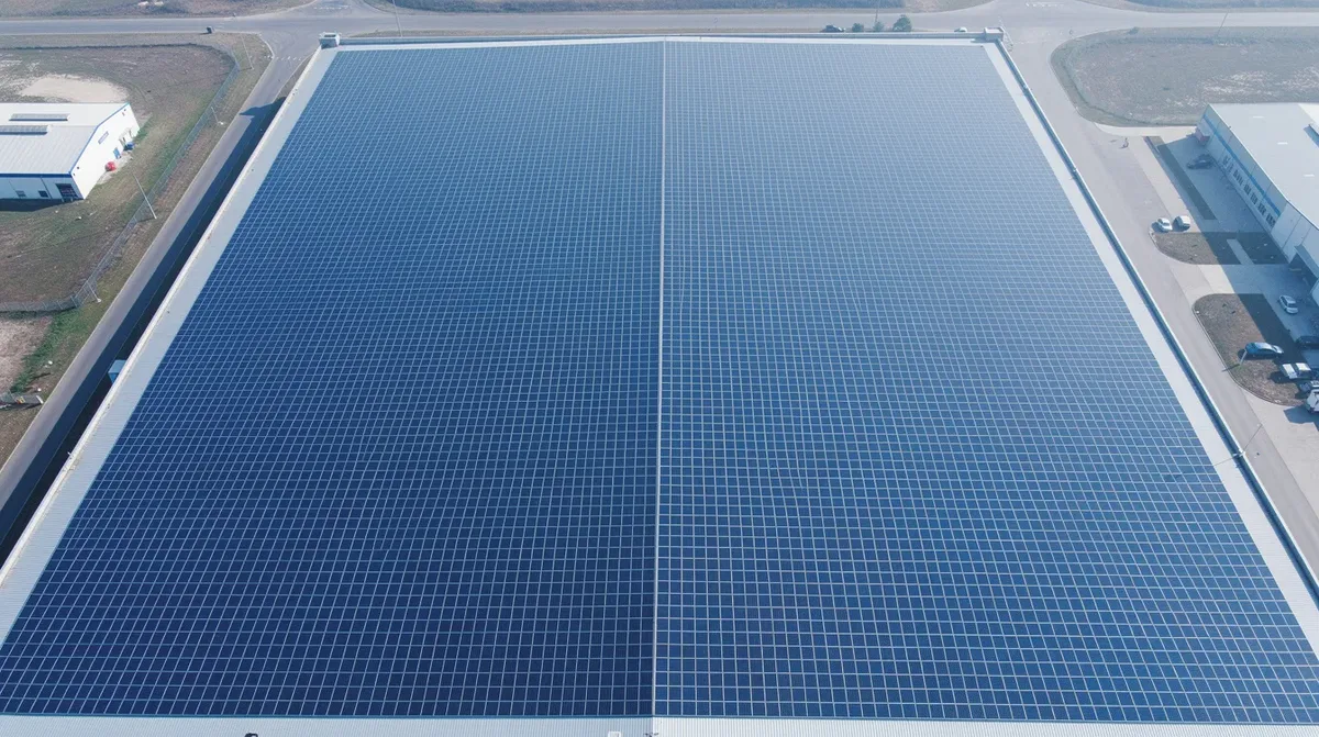 Vue du ciel, un grand toit industriel dans le canton de Neuchâtel est entièrement recouvert de panneaux solaires photovoltaïques, illustrant l'engagement vers les énergies renouvelables et la neutralité carbone. Cette installation clé en main témoigne des efforts pour lutter contre le changement climatique et favoriser l'autoconsommation.